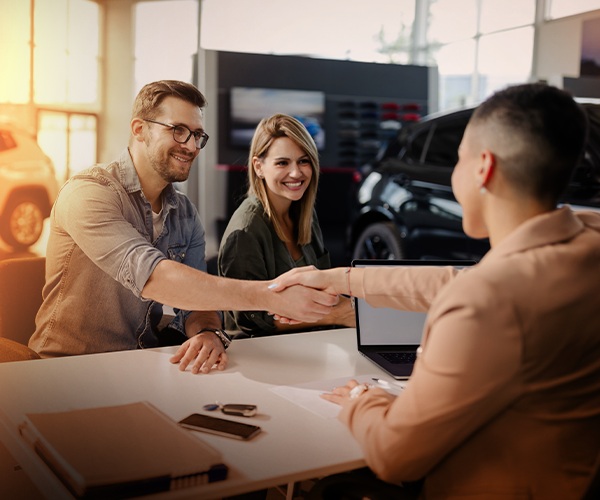 Couple buying a vehicle at dealership and shaking hands